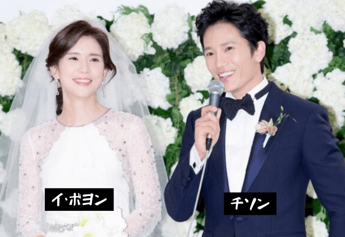 韓国女優イ・ボヨンと韓国俳優チソンの結婚当時の画像。左側に白のウエディングドレス姿のイ・ボヨン、右側にネイビーのタキシード姿のチソン。チソンがマイクを持ってインタビューに答えている。